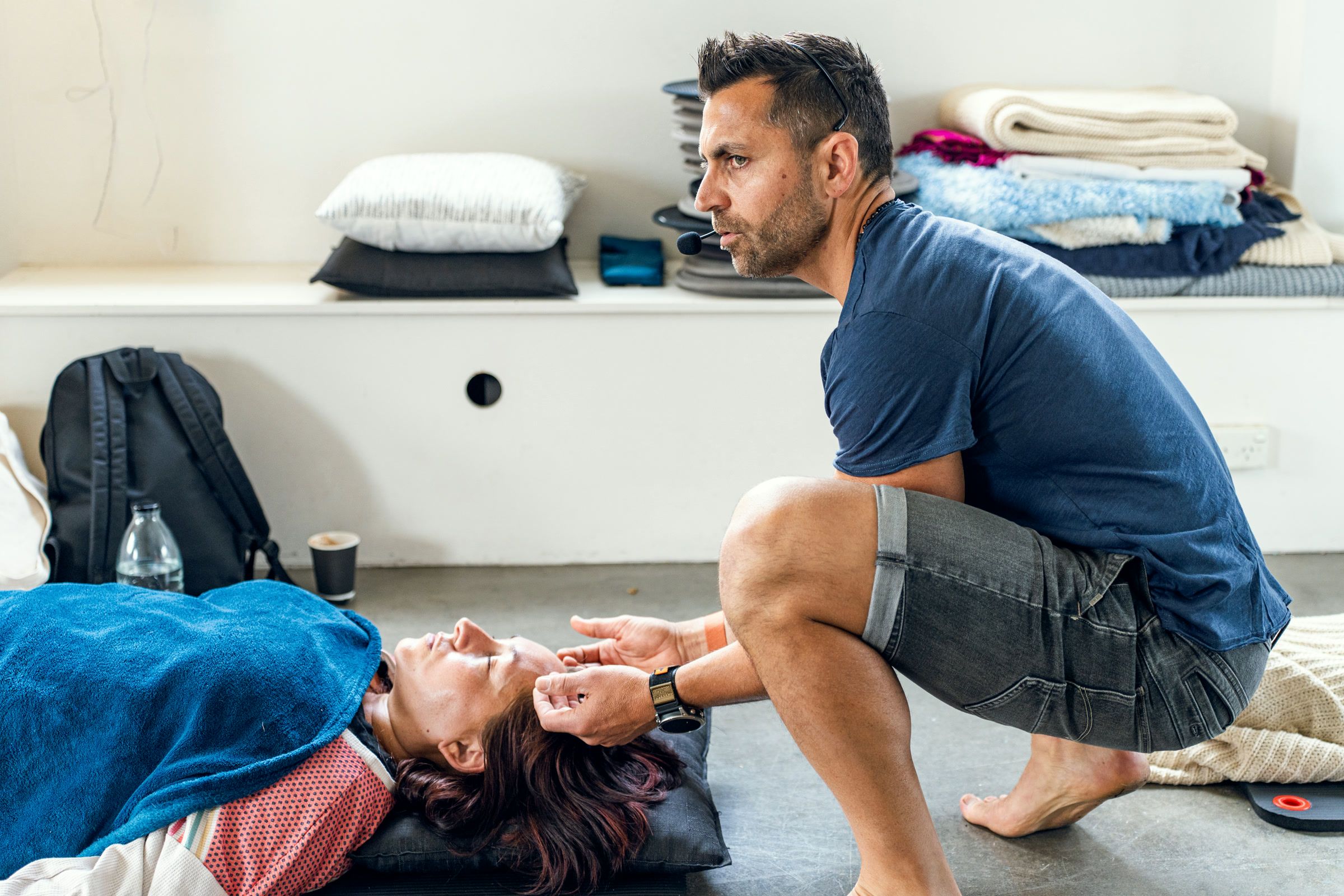 Dino crouching beside a woman lying down, his hands lightly on her head as she breathes.