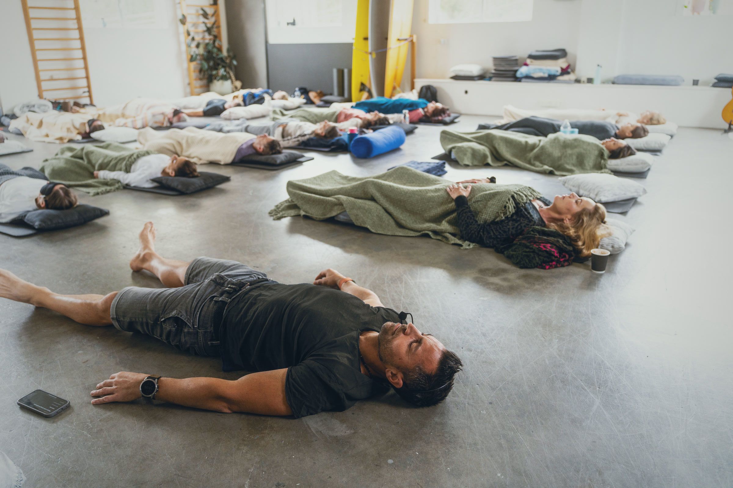 Dino lying on the studio floor among a group, everyone resting with eyes closed after a session.